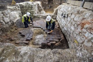 MOLA archaeologists excavate the top of the cesspit, which had been backfilled and covered over with several layers of brick flooring.