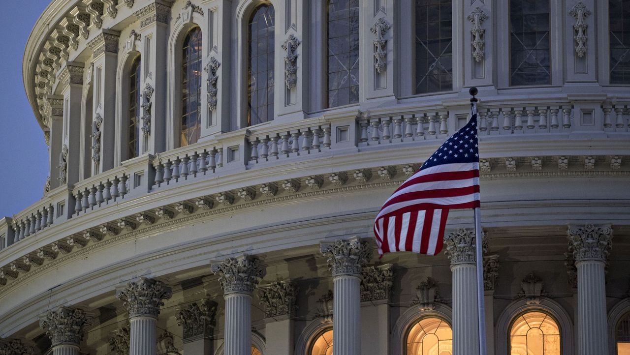 An American flag on a pole outside the Capitol building at dusk. 