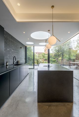 a stylish, minimalist kitchen extension by Ar'Chic - with black/grey units, a large black/grey island, slate floors and wrap around floor-to-ceiling doors/windows