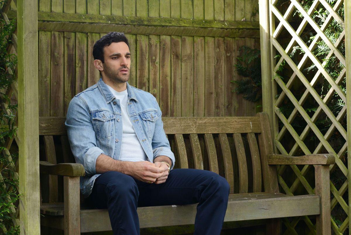 EastEnders Kush Kazemi sitting on a bench.