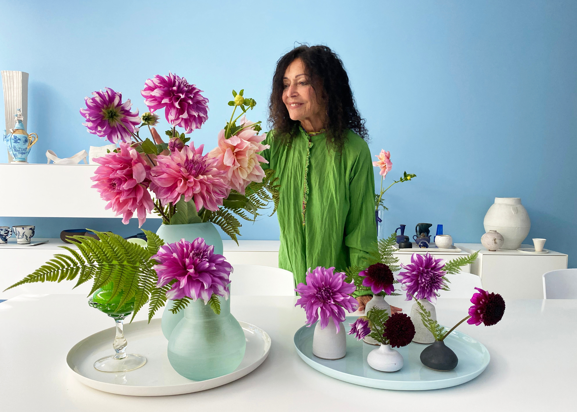 A woman in a green top arranging pink and purple dahlia in vases on a tray