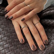 A woman's hand with a chocolate brown manicure placed on top of a matching brown handbag