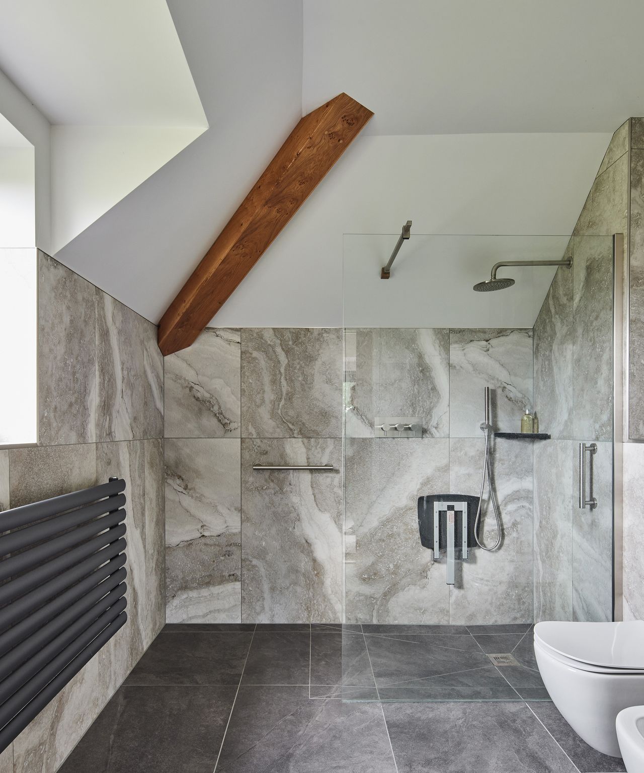 A walk in shower in a bathroom with grey tiles