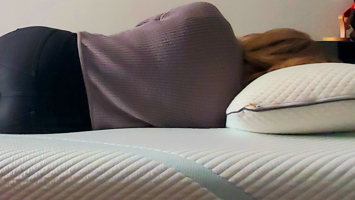 Image of our lead mattress tester, wearing a purple top and black trousers, lying on the Tempur-Pedic Tempur-Adapt mattress