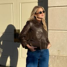 A woman wearing a brown leather jacket and sunglasses