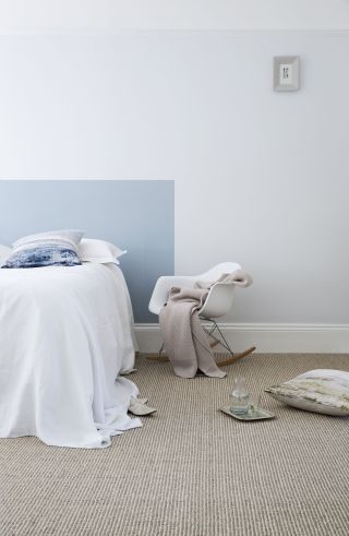 A blue bedroom with DIY painted headboard, with a beige jute carpet and a white chair, and accessories on the floor