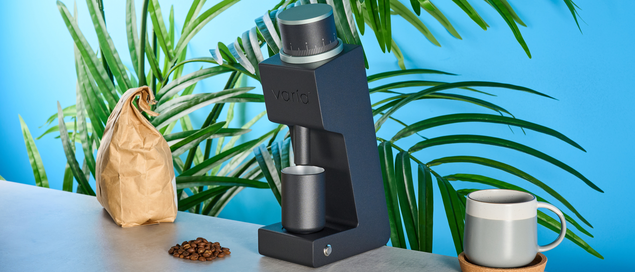 The Varia VS3 coffee grinder in use on a stone surface with a blue background