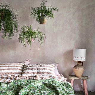 Grey bedroom with bed, lamp, and three plants hanging from ceiling
