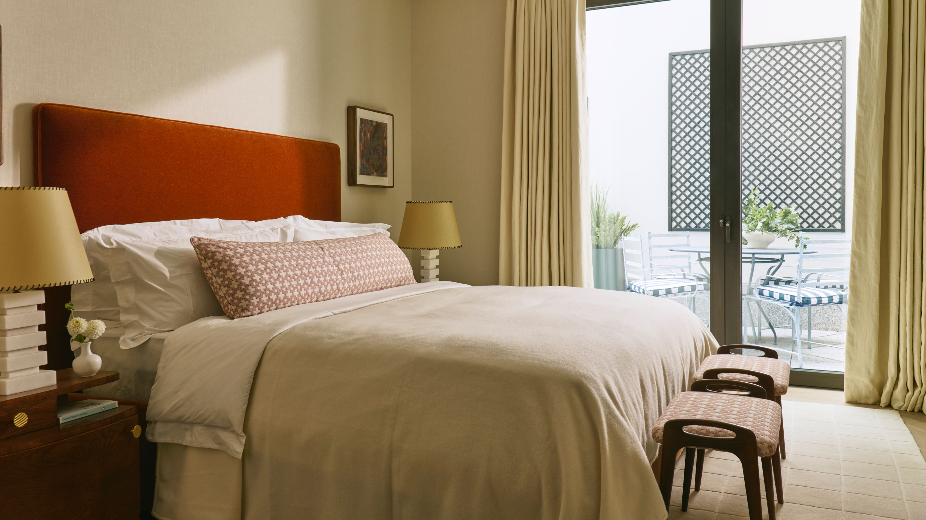a creamy primary bedroom with patio doors and a rust red headboard