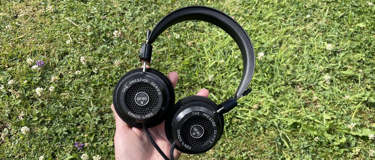 Becca&#039;s hand holding the Grado SR80x headphones against some grass