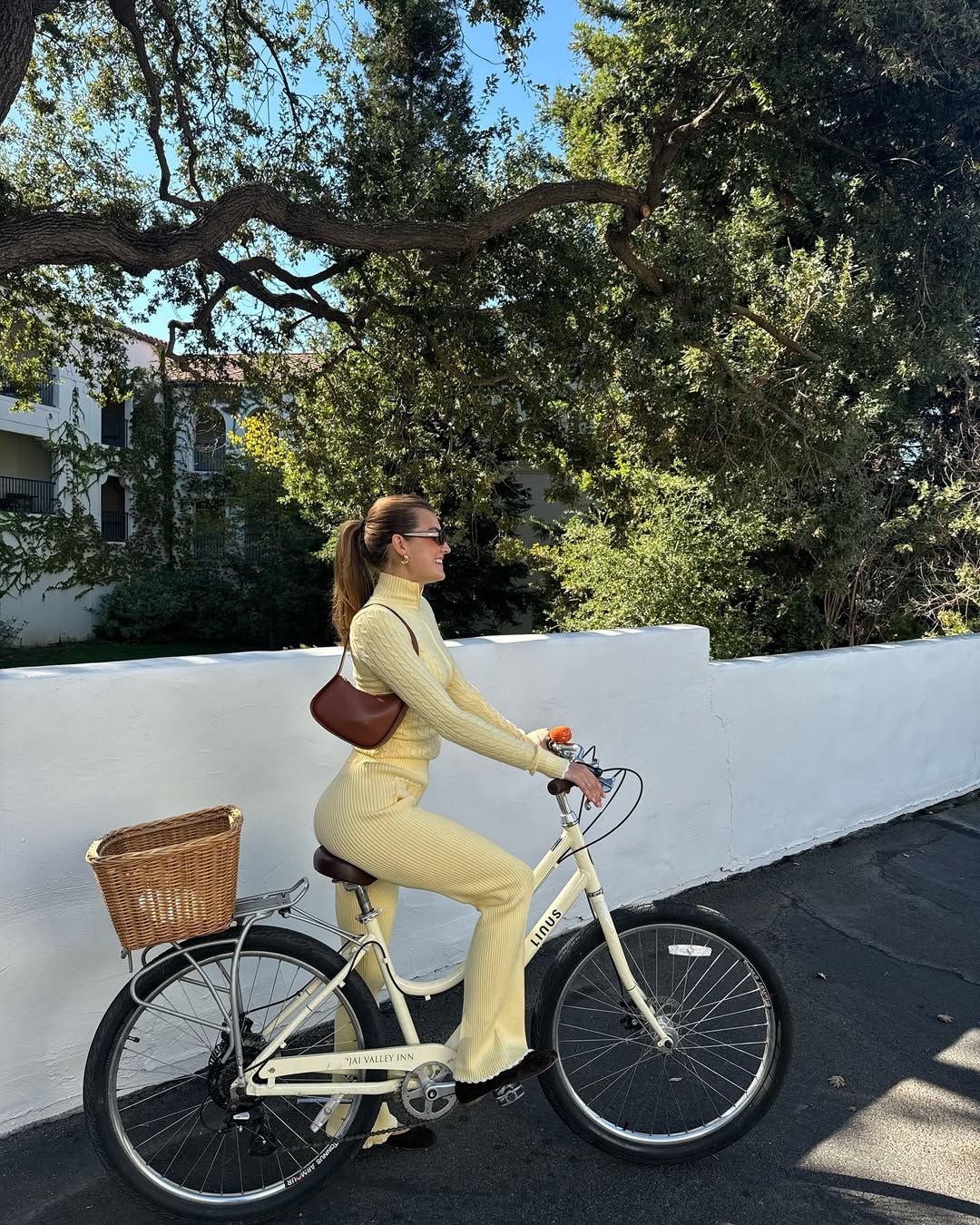 Styledsara in a matching butter yellow set riding a yellow bicycle and carrying a brown bag .