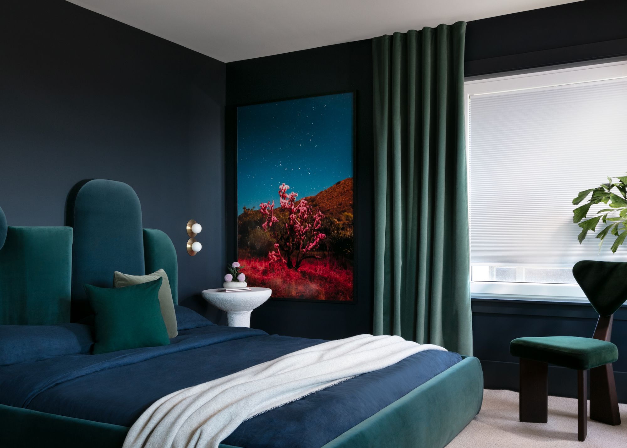 A bedroom with dark blue walls, a blue-green bed and an emerald chair