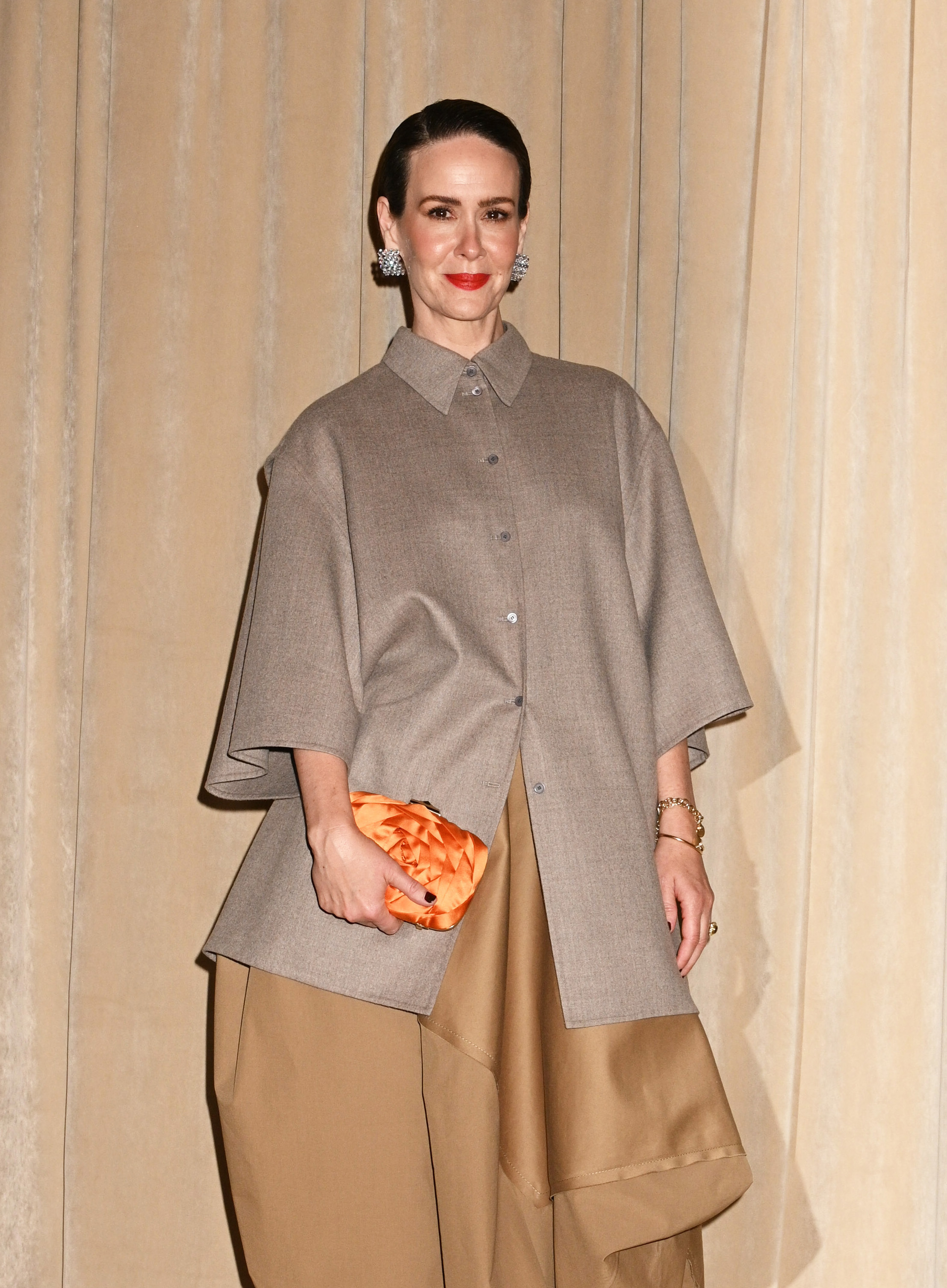 a white woman with short hair wearing an oversized shirt and pants and posing in front of a cream background