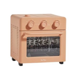 A square shaped air fryer and toaster in a warm terracotta color, with three knbs, a window showing a silver oven rack, and black feet