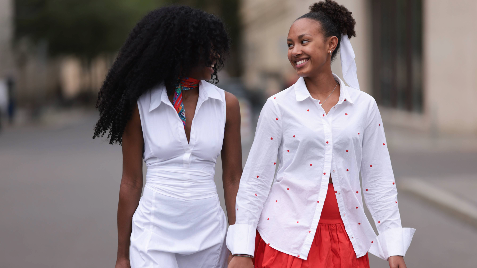 BERLIN, GERMANY - JULY 03: Lilian Litehiser (left) is seen wearing a red scarf with a multi-colored abstract pattern from Roeckel, a sleeveless white midi dress with a collar and accentuated waist from Banana Republic and a red leather bag from Chanel. Her daughter Morena (right) is seen wearing small silver hoop earrings and stud earrings; a silver necklace with a heart pendant; a white hairband; a white long-sleeved shirt with a red heart pattern from Oui; a high-waisted, red, mini balloon skirt with ruffled seam from H&M; and a squared, wooden, vintage handbag with a print of a woman and black bamboo handle during the Berlin Fashion Week SS25 on July 03, 2024 in Berlin, Germany. (Photo by Jeremy Moeller/Getty Images)