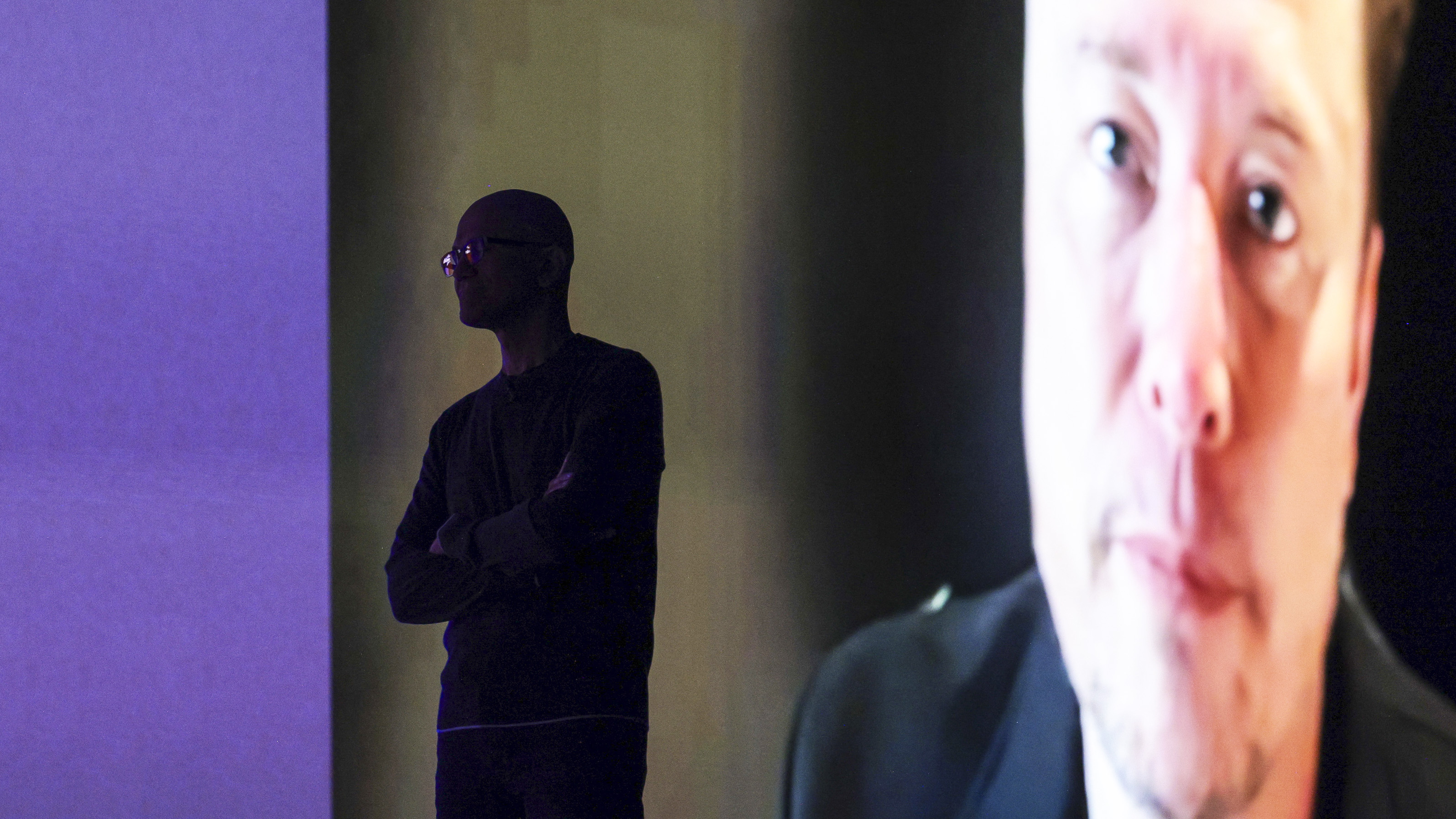 Microsoft Chairman and Chief Executive Officer Satya Nadella (L) is silhouetted as a pre-recorded interview with Elon Musk is played after announcing that Grok AI, by Musk's artificial intelligence start up xAI, will be available on Microsoft's Foundry Models, during the Microsoft Build conference opening keynote in Seattle, Washington on May 19, 2025. (Photo by Jason Redmond / AFP) (Photo by JASON REDMOND/AFP via Getty Images)