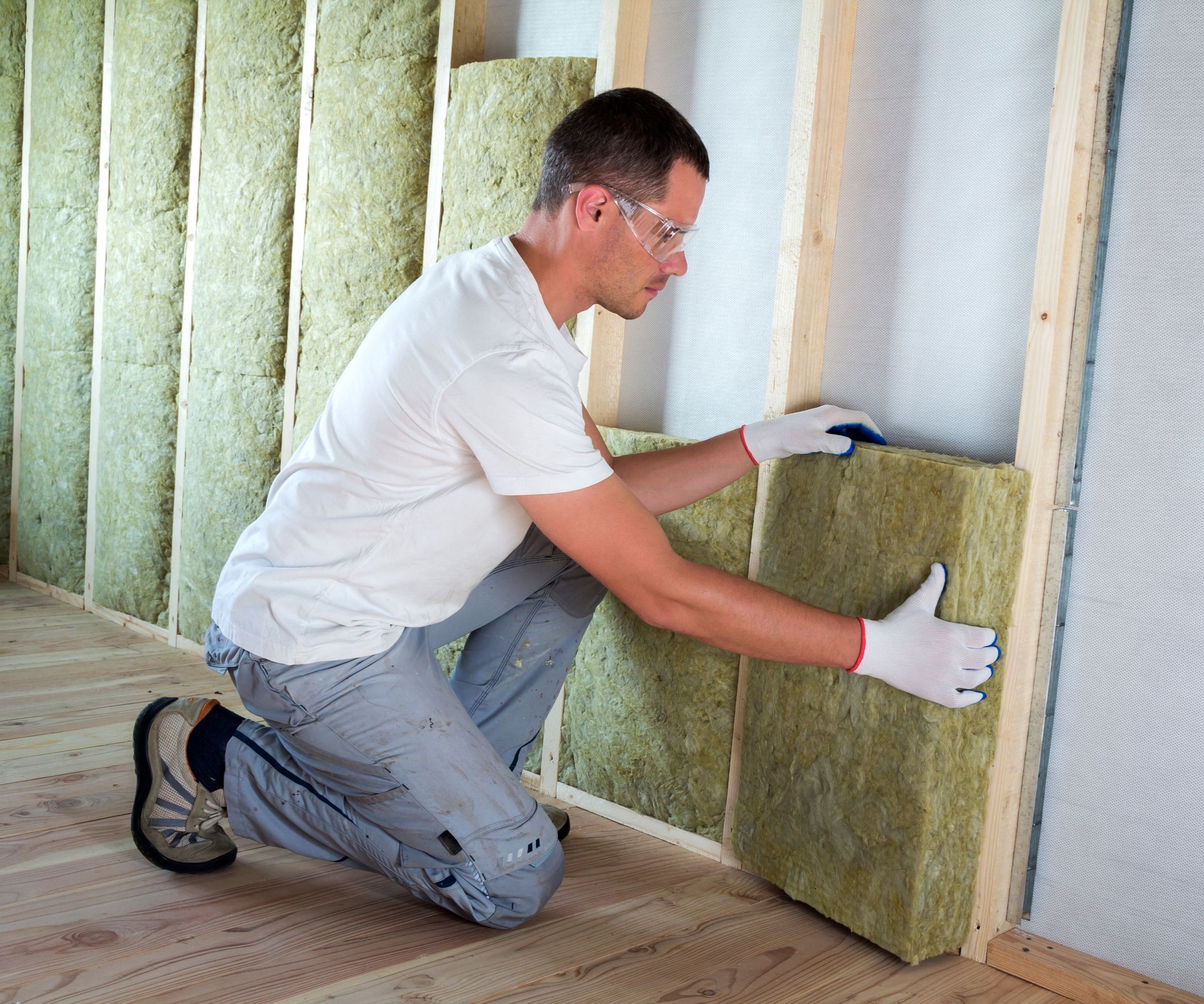 A man in a white T-shirt installing insulation in a wall