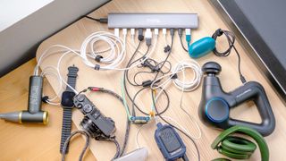 Plugable PS-10CC 10-port USB-C charging hub in use on a wood desk with a range of accessories plugged in including earbuds, smartwatches and a digital camera