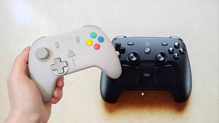 Hand holding Retro Fighters StrikerDC Dreamcast controller next to Valve Steam Controller on screen in backdrop.