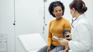 Woman having her blood pressure checked with machine by doctor during NHS Health Check