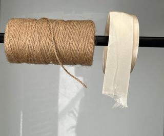 A black tension rod hanging in a cabinet holding two reels of string and ribbon