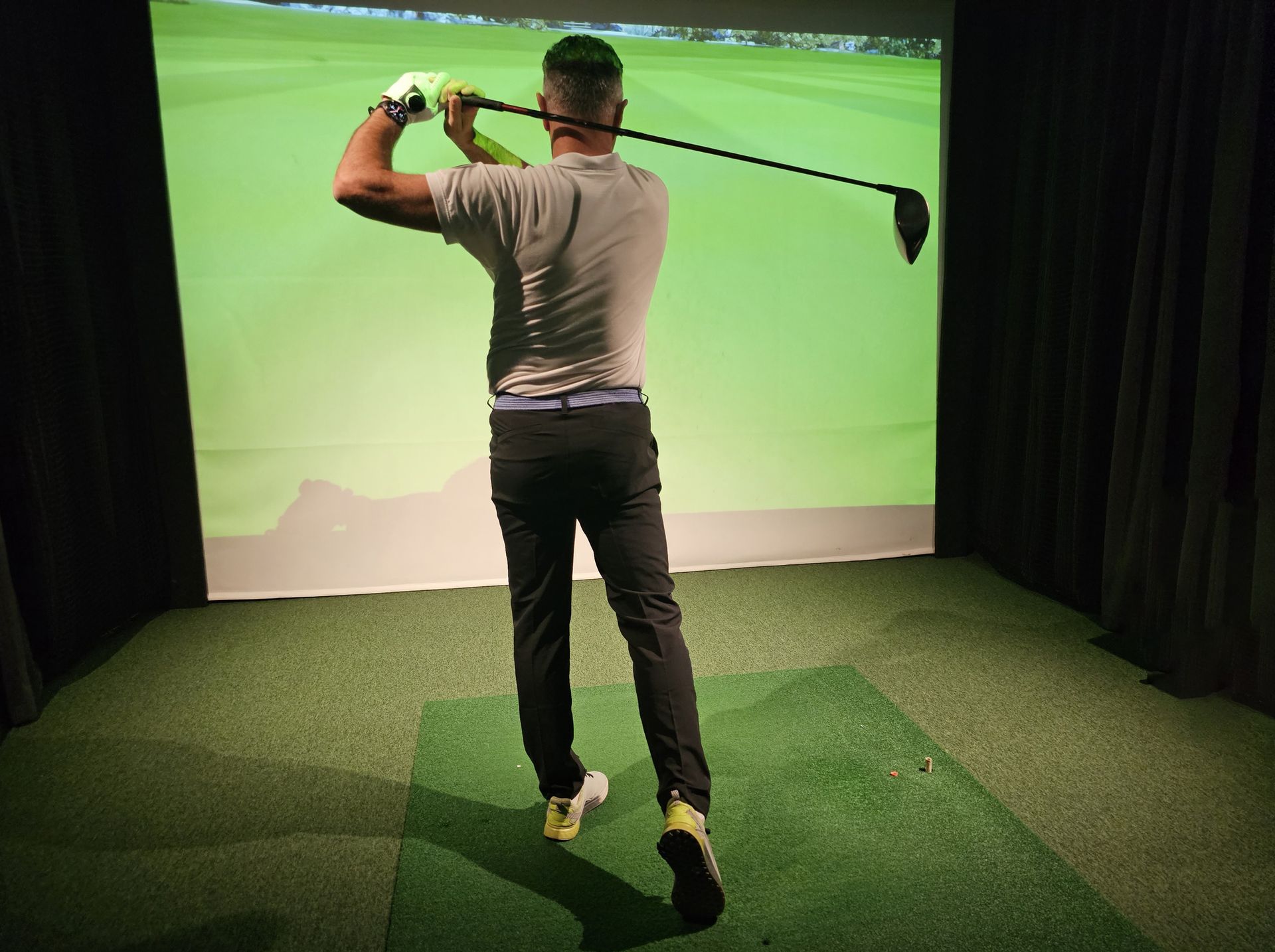 Professional male golfer holding club playing golf indoors on golf simulator