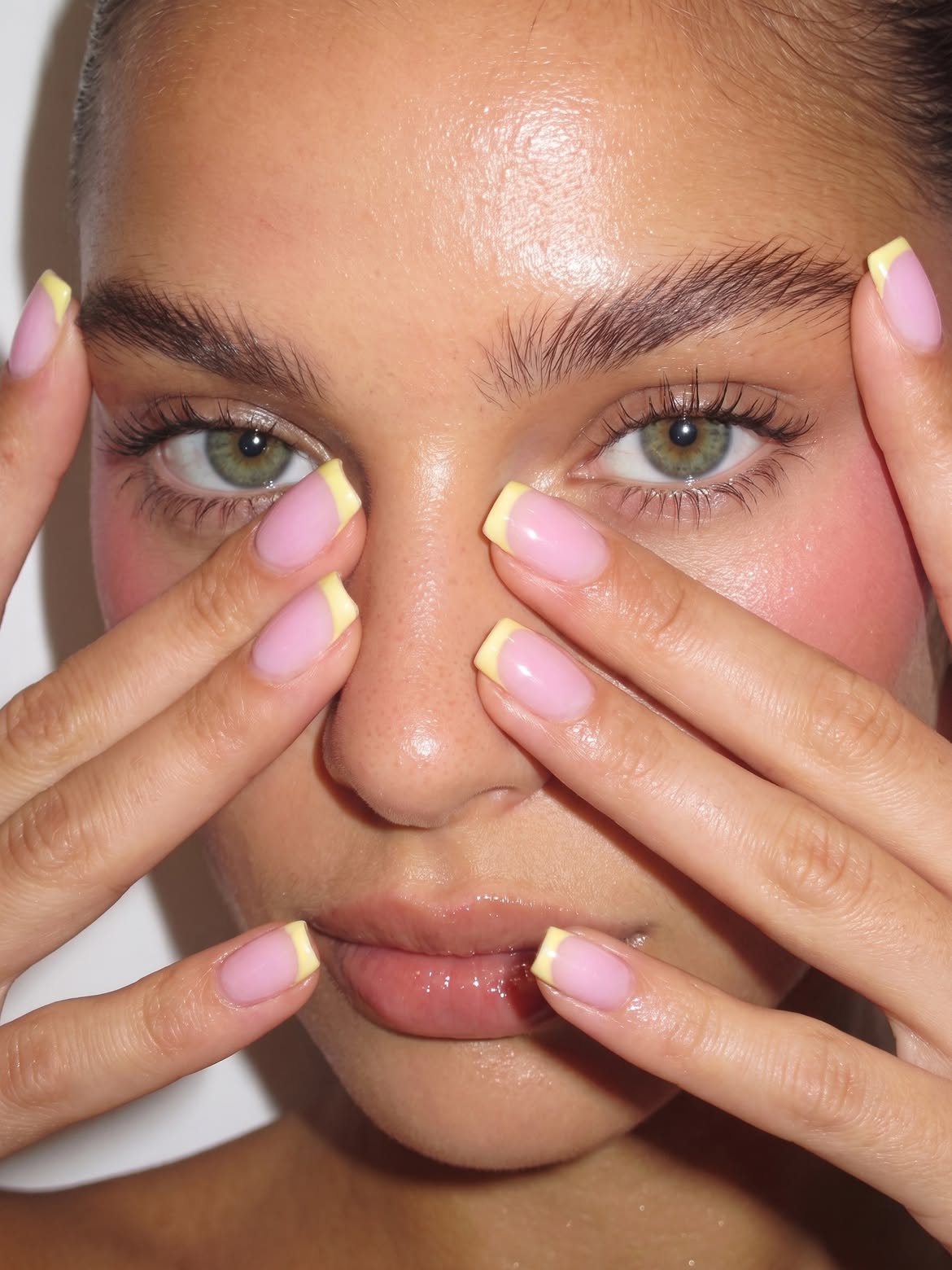 a girl holding up her square nails with a sheer pink base and thick buttery yellow French tips