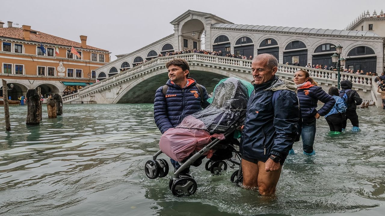VENICE, ITALY - OCTOBER 29: Tourists carry a stroller through the flood waters on October 29, 2018 in Venice, Italy. Today due to the exceptional level of the "acqua alta" that reaced 156 cm