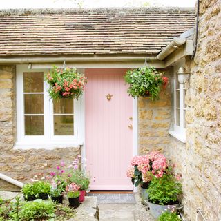pathway leading to a pink cottage door with hanging baskets either side