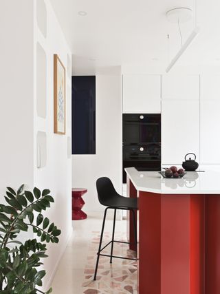 An all white kitchen with a bright red island