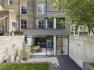 a double storey flat extension with terraced brick buildings in the background and a stylish kitchen extension in the foreground, leading onto a decking and garden space