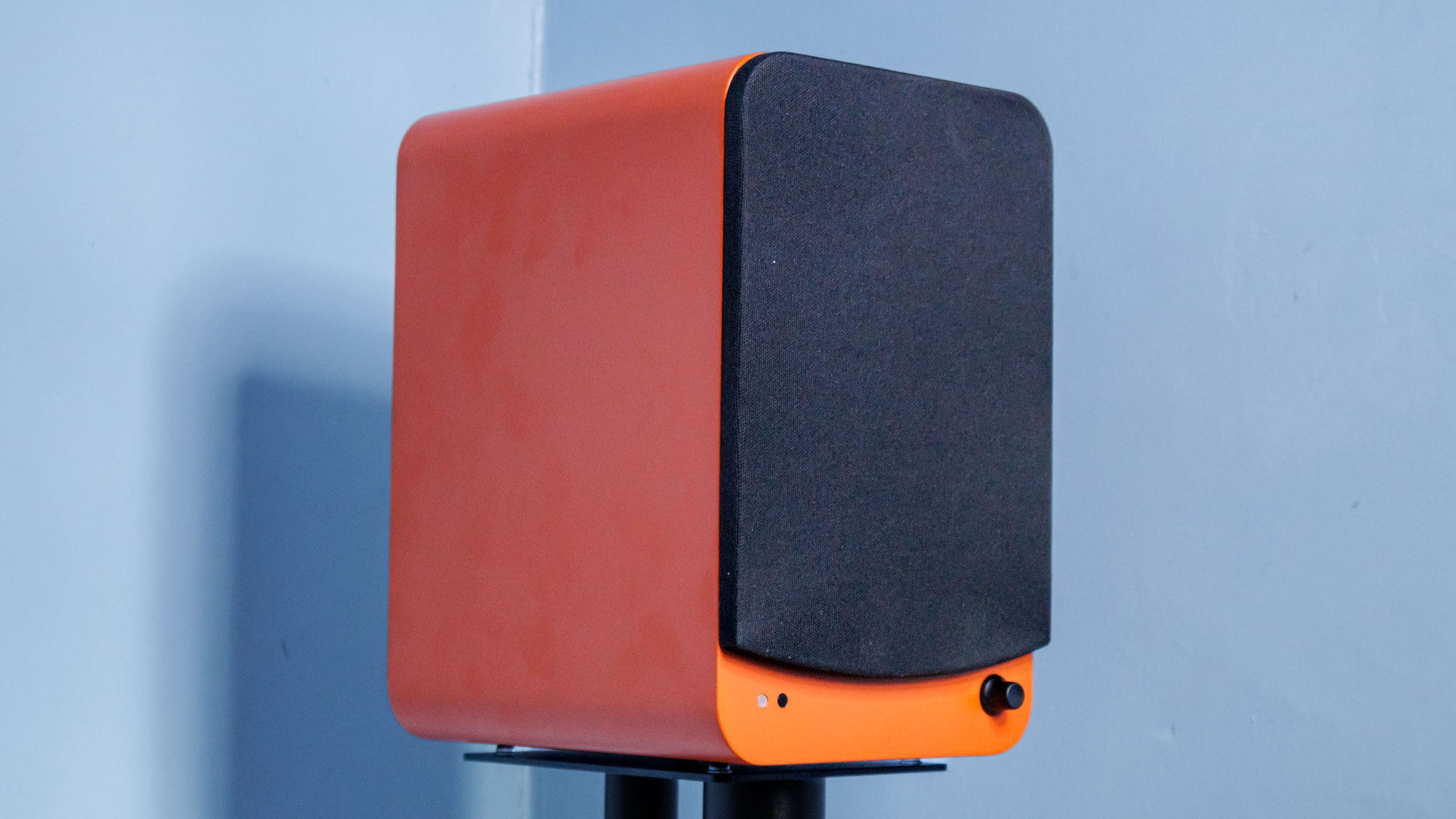 Orange Kanto Ren speaker in front of a blue wall with the speaker grille attached