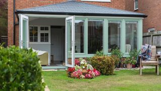 conservatory with black solid tiled roof and green frame on back of house