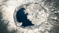 Satellite photo of a sow covered volcano with a larger crater filled with a lake and lava flows that make it look like a yin-yang symbol