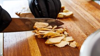 close up of a person's gloved hands as they slice through a lab-grown chicken breast with a knife on a cutting board