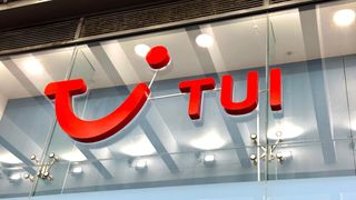 Telephoto shot of the TUI logo on a glass wall. Decorative: the TUI logo is the word 'TUI' next to a stylized smile, in red.