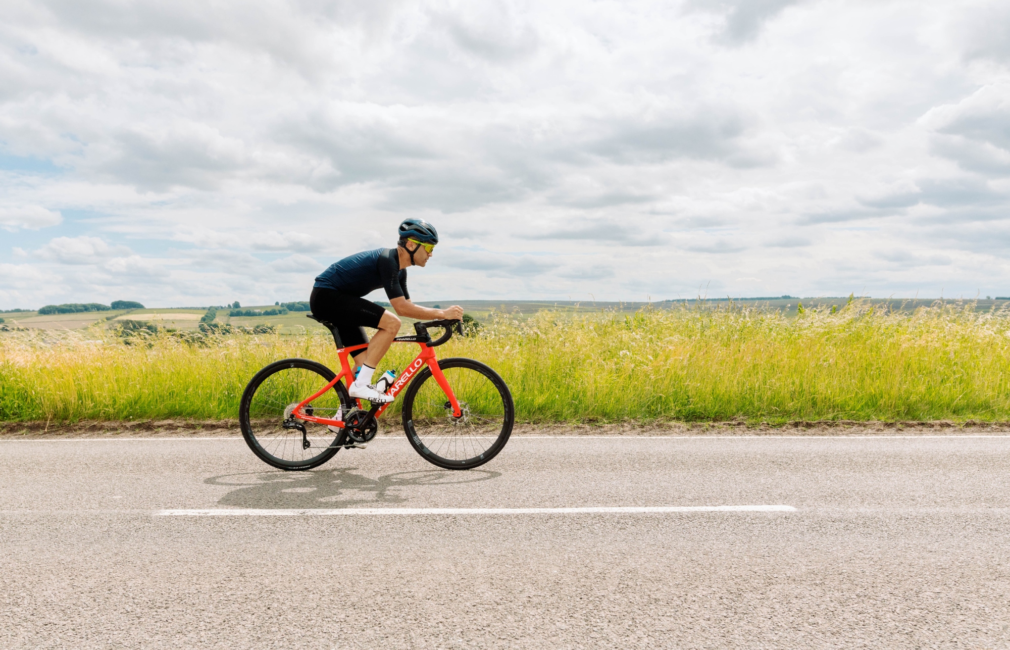 A male cyclist on a Pinarello X riding ona  flat road with a field of grass behind them
