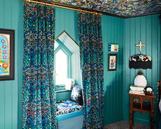 Bright blue bedroom with cozy window seat near small arched window, patterned floral curtains