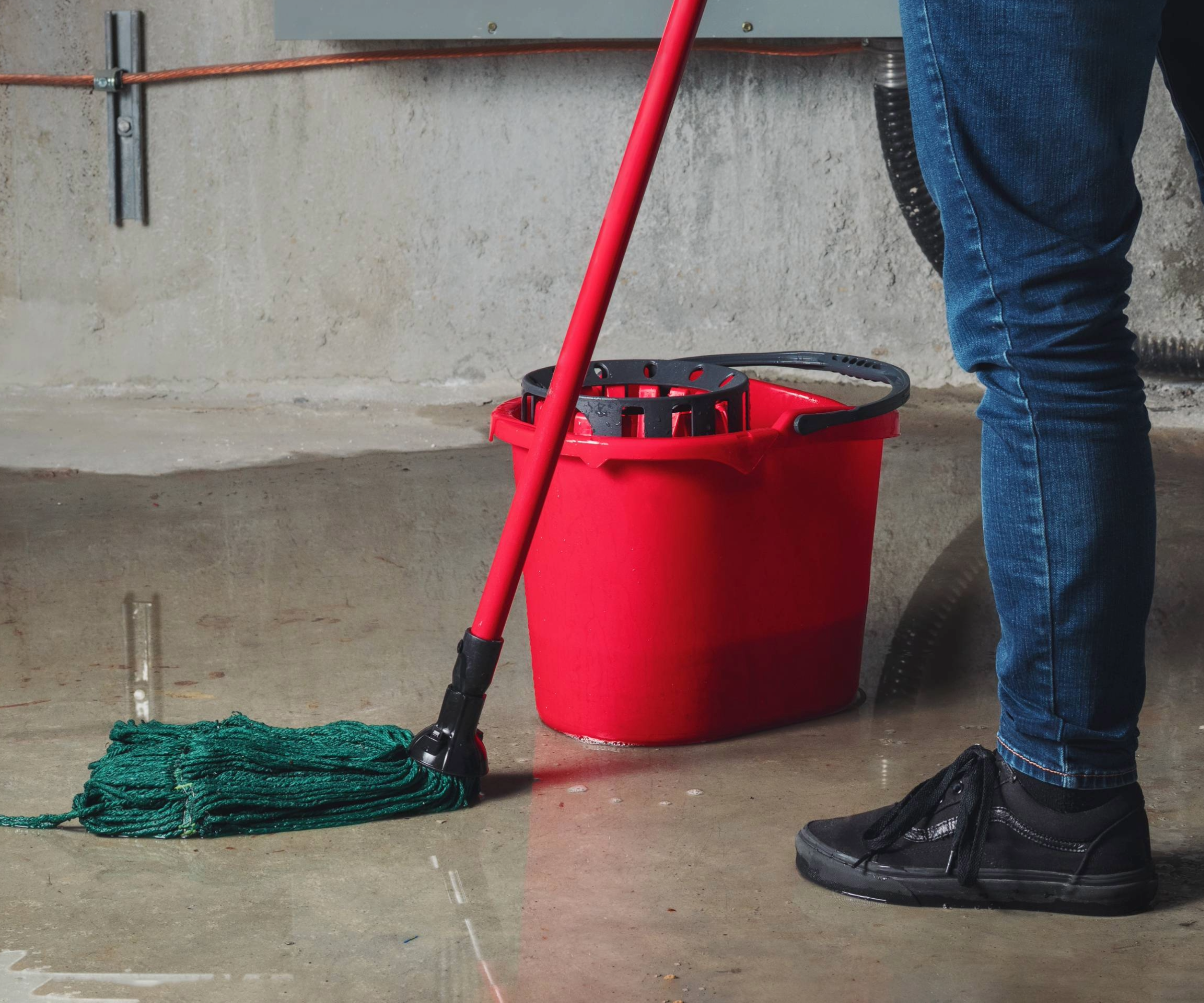 Lower half of a person using a red mop and bucket on a wet floor