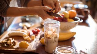 Woman cutting up banana and other fruits into a blender to make healthy pre-workout shake