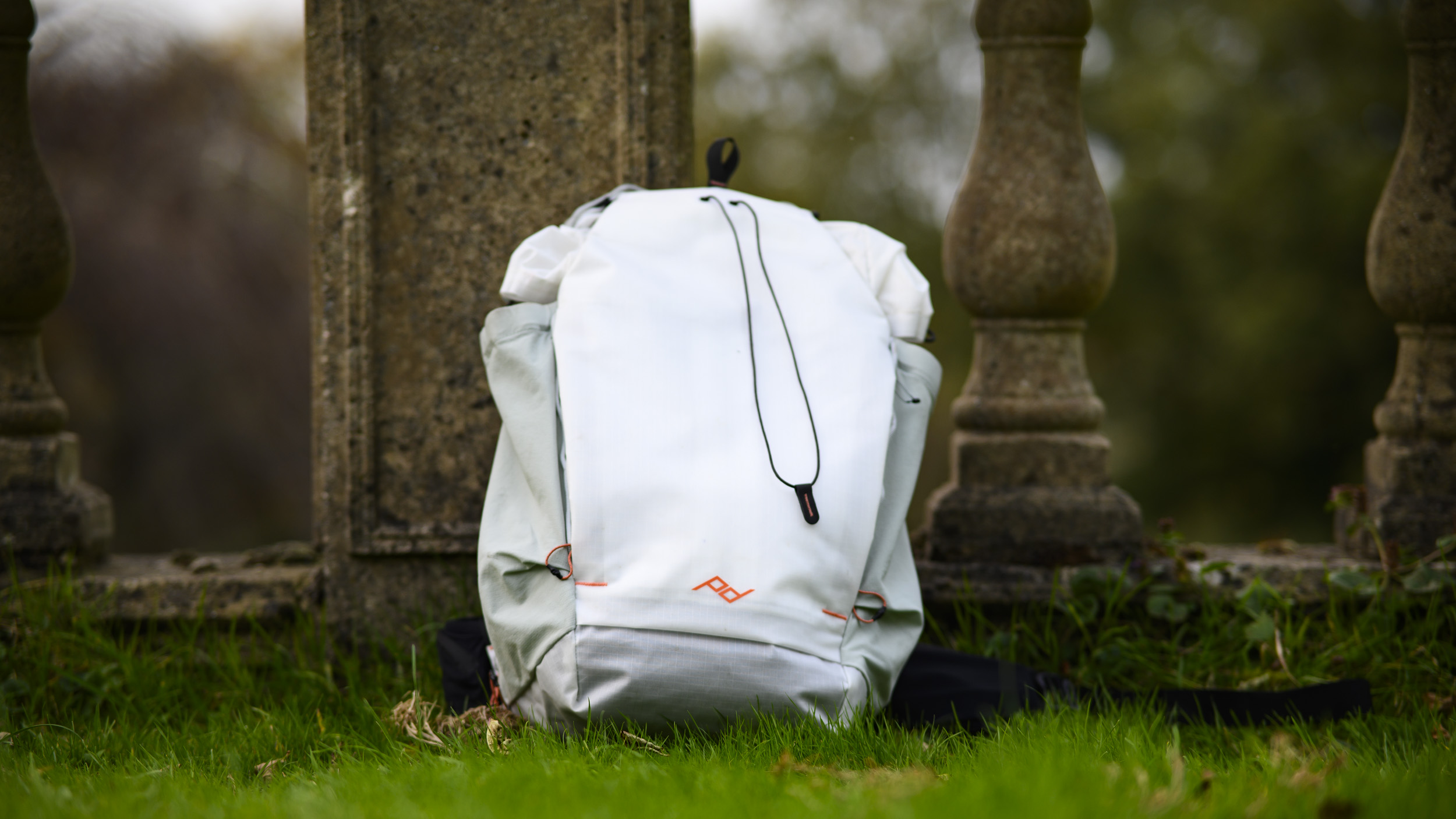 Peak Design Outdoor Backpack 25L in white, on the grass by concrete posts