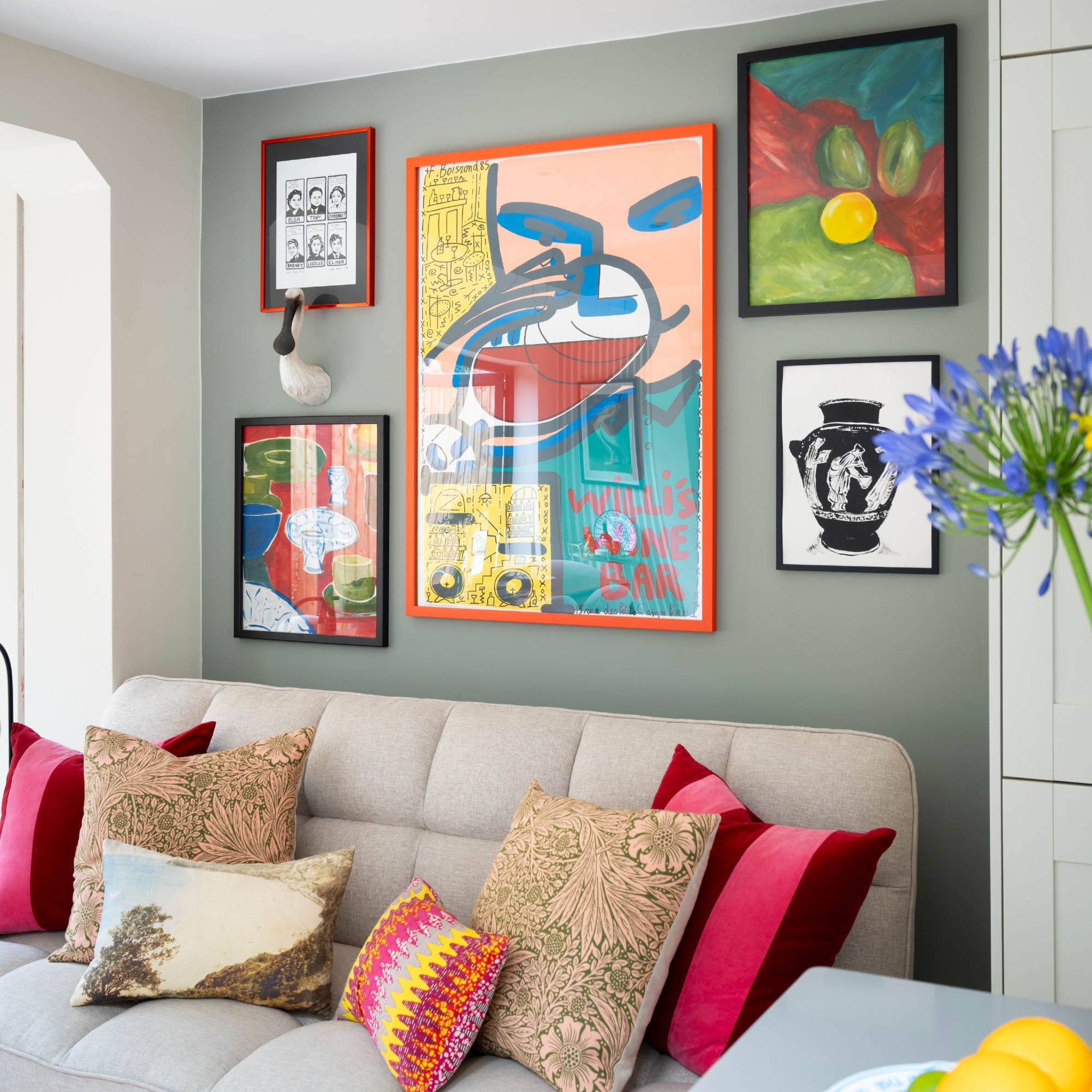 A living room with a feature wall painted in sage green and covered with a colourful gallery wall with a cream sofa underneath it