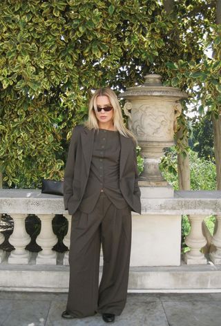 a photo of a woman wearing a classic outfit with an olive green blazer and matching waistcoat and trousers styled with tabi ballet flats