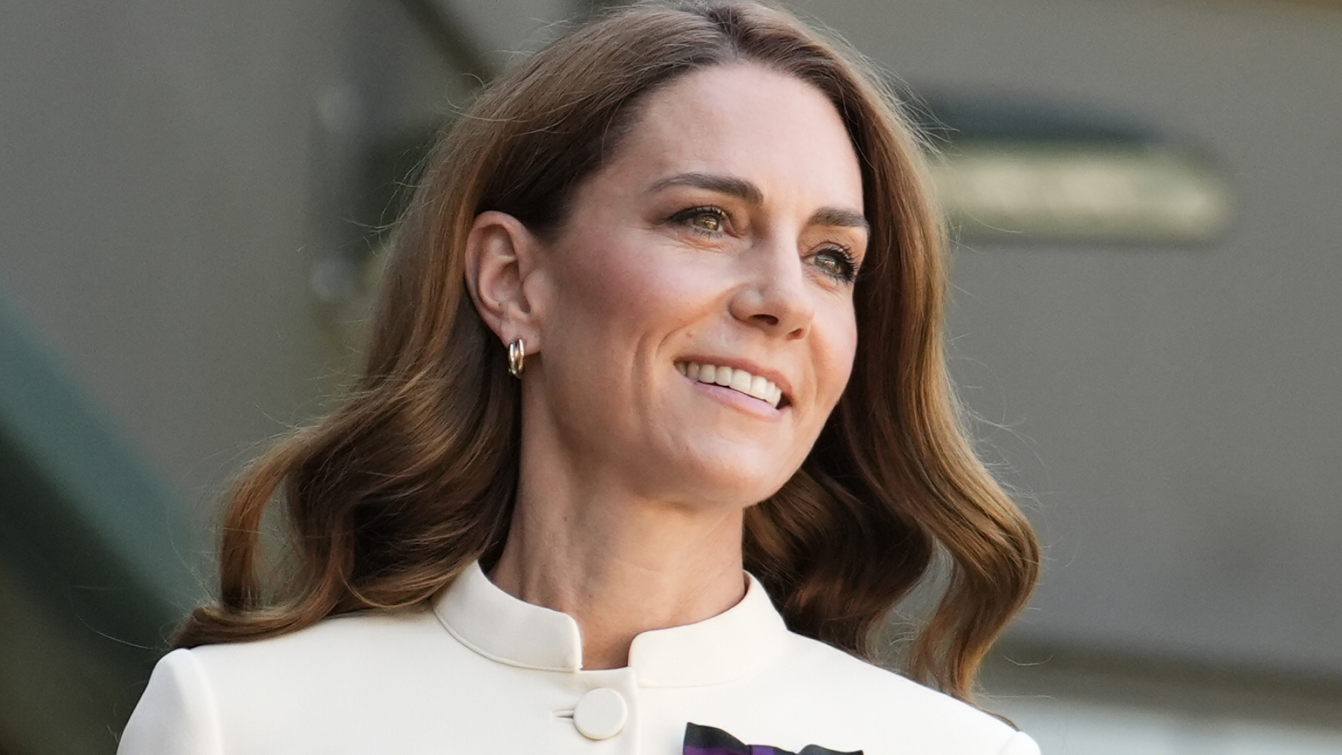 Kate Middleton has long brown wavy hair and wears a white dress