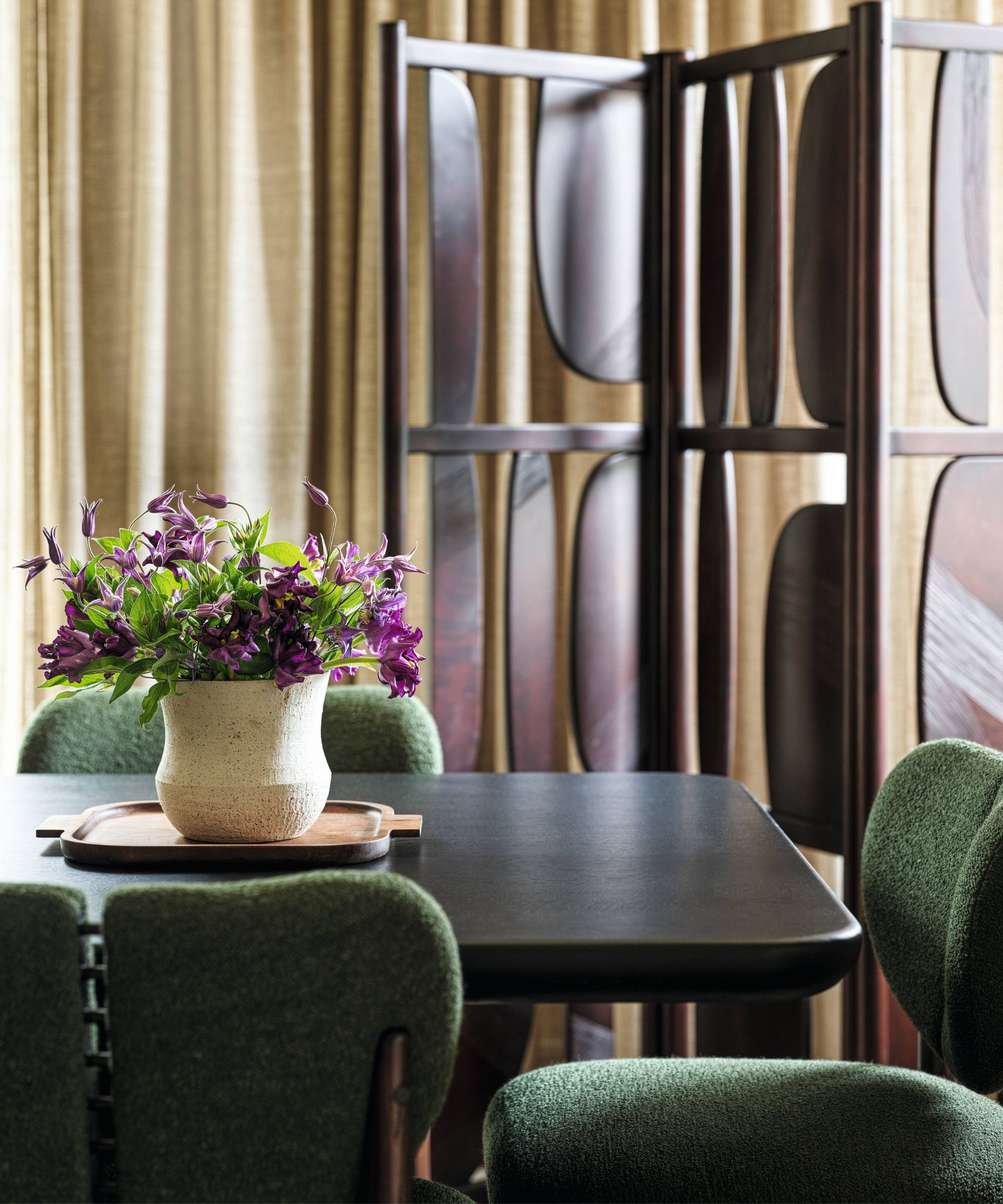a close up shot of a dining room with a dark wooden screen, a dark dining table and green boucle chairs