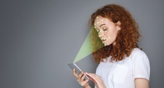 A woman looks at her phone to scan her face using facial recognition technology