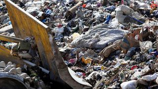 A digger pushing a discarded mattress in a pile of rubbish in landfill