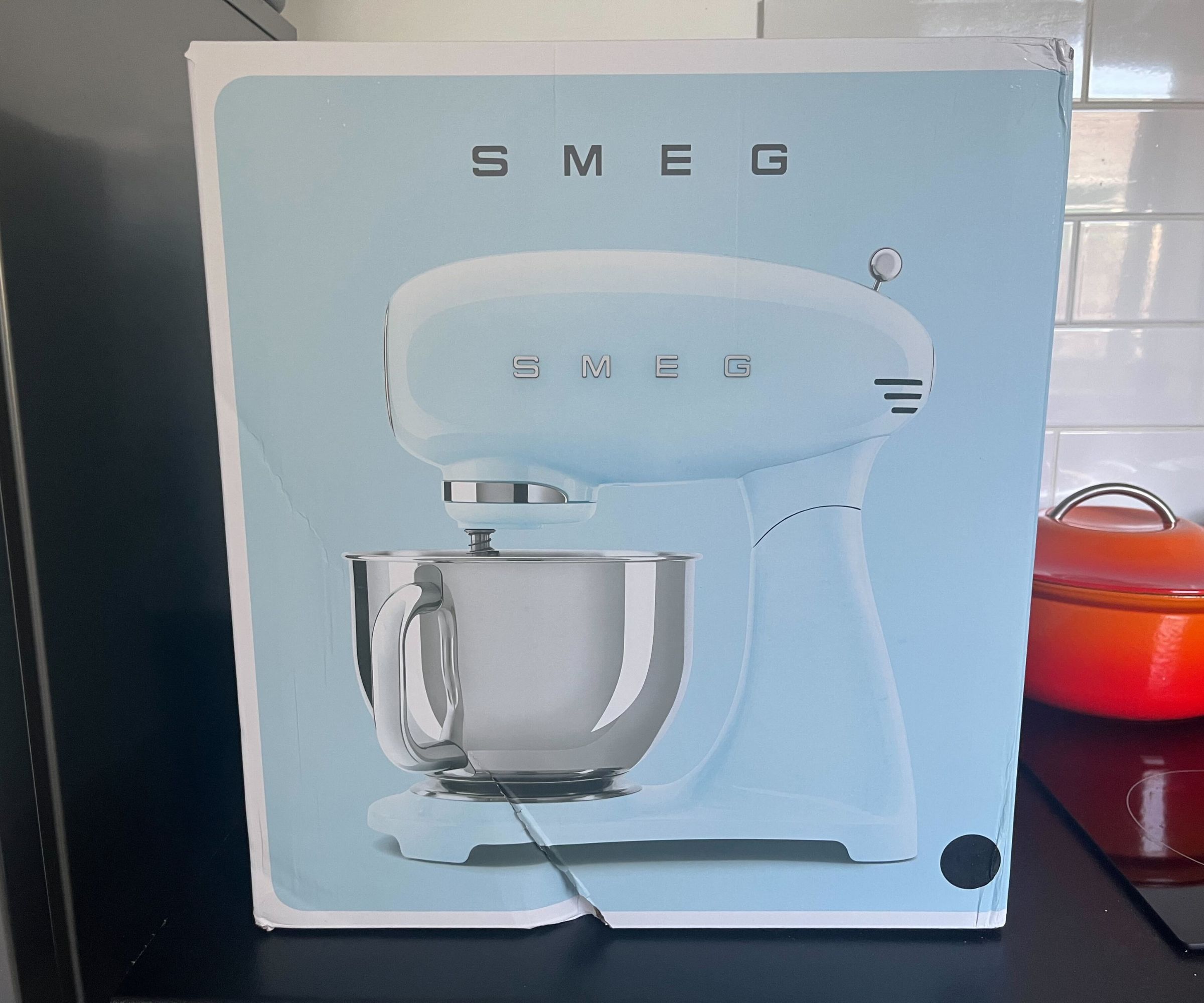 A baby blue SMEG Forte stand mixer box on a black kitchen counter