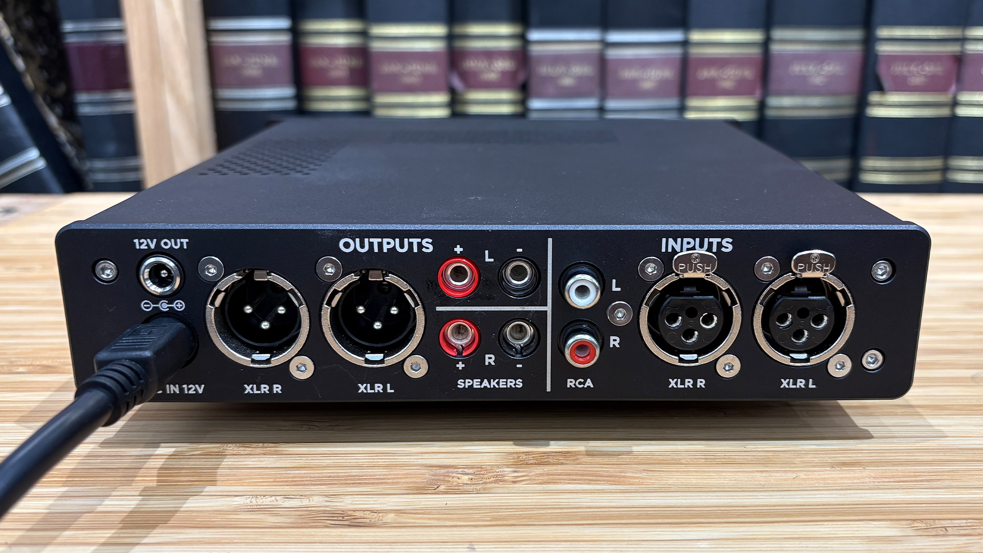 Chord Electronics Alto headphone amp on wooden surface in front of bookcase, rear of device showing connections