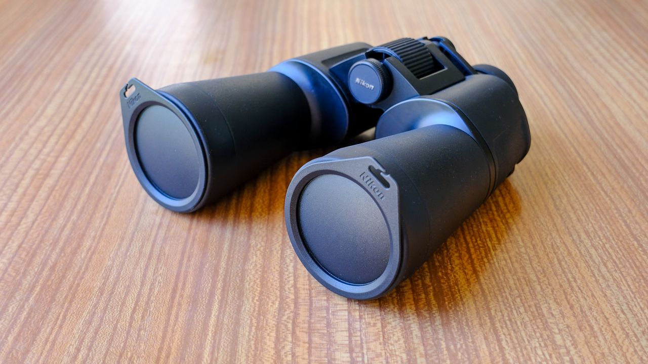 The Nikon Action 16x50 binoculars on a wooden table, with lens caps on.